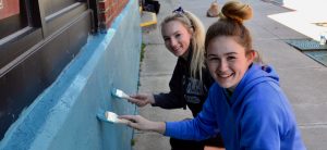 two teen girls smiling painting a wall blue