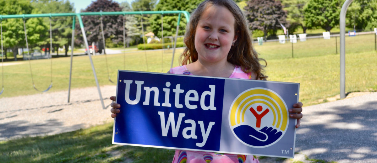 girl holding united way sign in front of playground