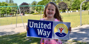 girl holding united way sign in front of playground